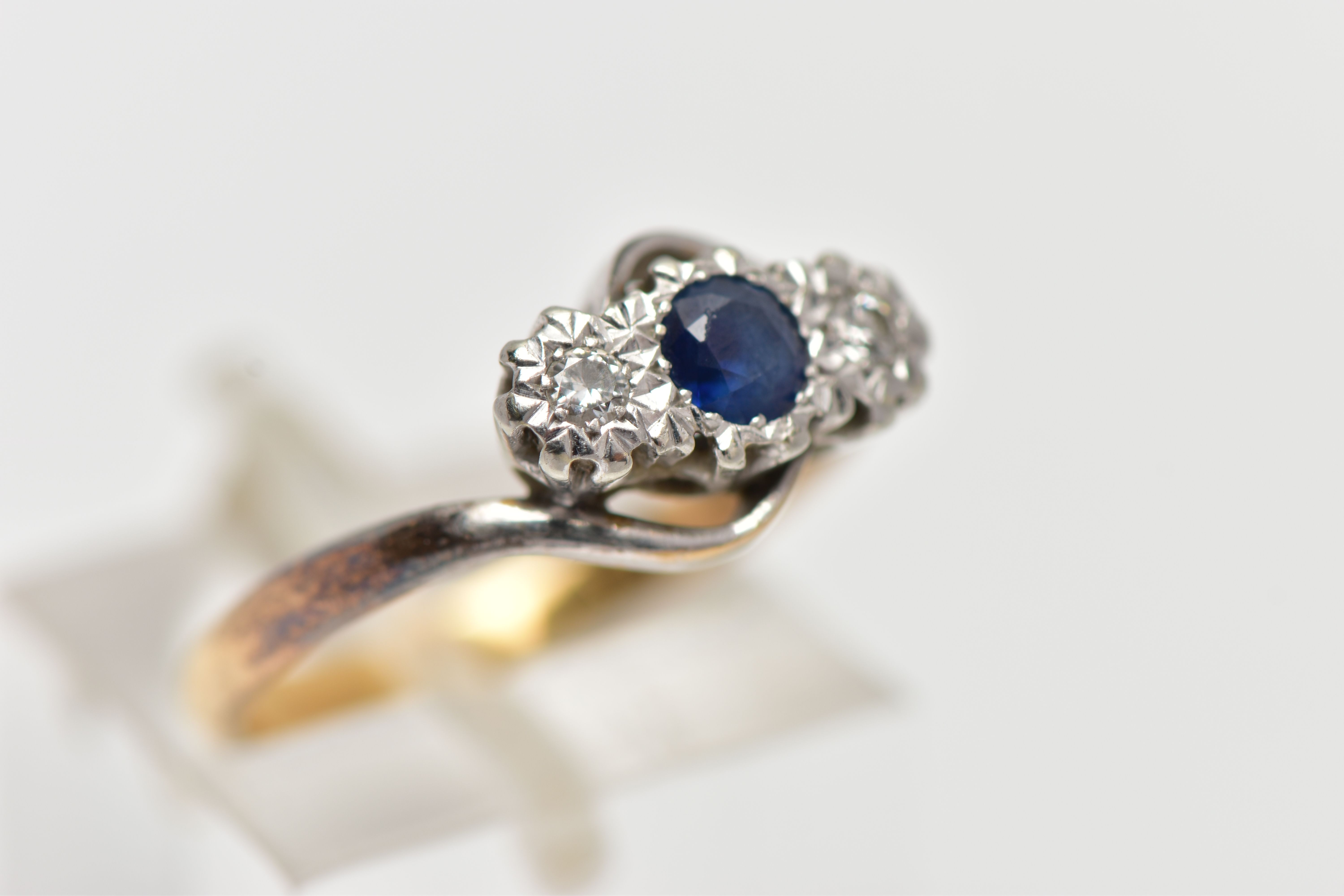 A YELLOW METAL CROSS OVER THREE STONE RING, designed with a central circular cut blue sapphire, - Image 4 of 4