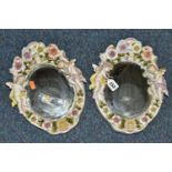 TWO OVAL WALL HANGING PORCELAIN FRAMED MIRRORS, the white porcelain frame is flower encrusted, two