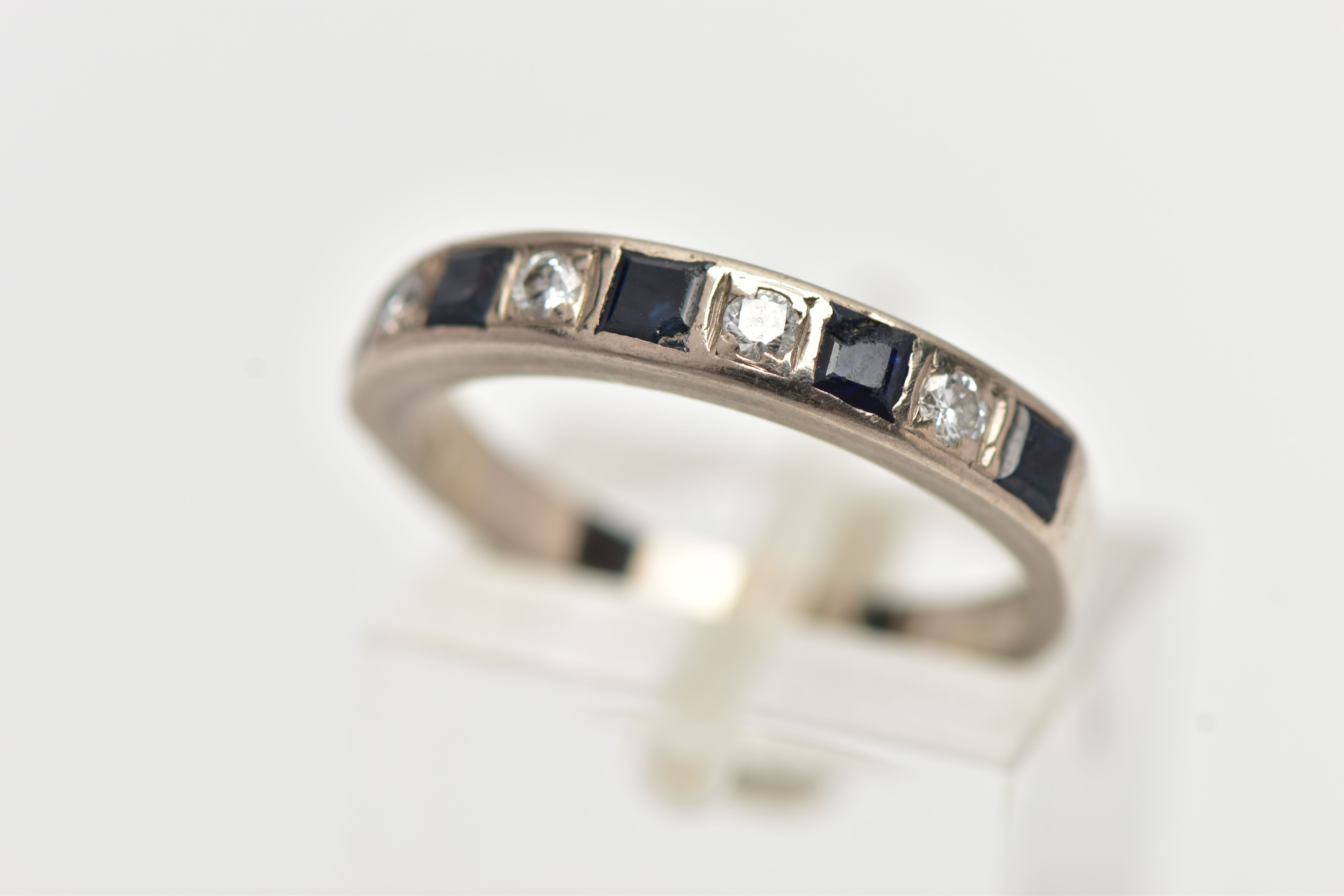 A WHITE METAL SAPPHIRE AND DIAMOND HALF ETERNITY BAND RING, set with four round brilliant cut