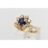 AN 18CT YELLOW GOLD SAPPHIRE AND DIAMOND CLUSTER RING, centering on a circular cut blue sapphire, in
