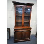 A VICTORIAN MAHOGANY BOOKCASE, with an overhanging cornice, two glazed doors, enclosing three