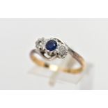 A YELLOW METAL CROSS OVER THREE STONE RING, designed with a central circular cut blue sapphire,
