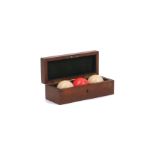 Three Edwardian ivory billiard balls, one stained red, in a mahogany case lined with green felt, the