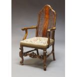 A walnut open armchair, early 20th century, with caned back, needlework seat and scroll arms above