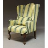 A George III style wing back armchair, circa 1900, with striped upholstery raised on carved mahogany