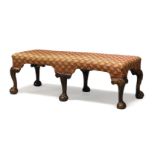 A George II stool, the rectangular seat with floral pattern fabric, on shell capped supports to claw