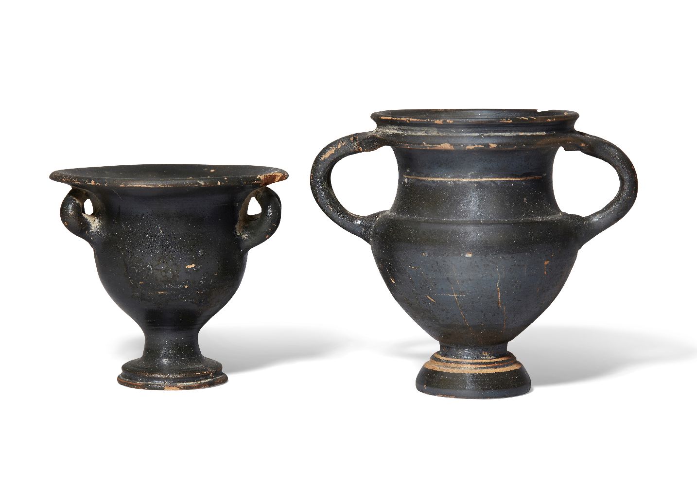 A black glazed kantharos on a pedestal base with two conjoined strips forming each handle, faint