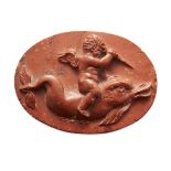 A pink stone carving of cupid riding a dolphin, of oval form and carved in high relief, Not Ancient,