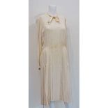 Chanel Couture, a cream collarless dress with ribbon tie at neck, concealed button front, full