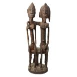 A Dogon seated couple, Mali, carved wood with encrusted patina, the two figures seated on a stool