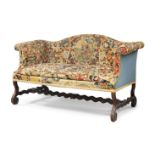 A Queen Anne oak framed camel back sofa, with tapestry upholstery, raised on scrolling supports,