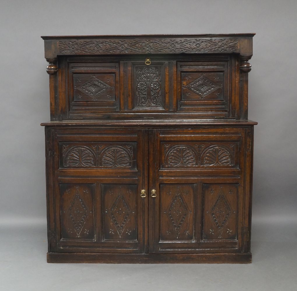 An oak court cupboard, 18th century and later, the carved frieze above carved fall front enclosing