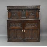 An oak court cupboard, 18th century and later, the carved frieze above carved fall front enclosing