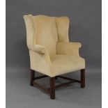 A George III style wing back armchair, upholstered in a cream fabric, raised on square legs joined