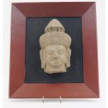 A Cambodian carved stone head, 20th century, mounted on a black board and in a red painted frame,