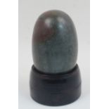 A polished lingam stone, of typical form, with associated carved and reeded wood stand, 21.5cm