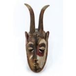 An African carved wooden mask, polychrome painted, with horns and pierced moth with carved teeth,