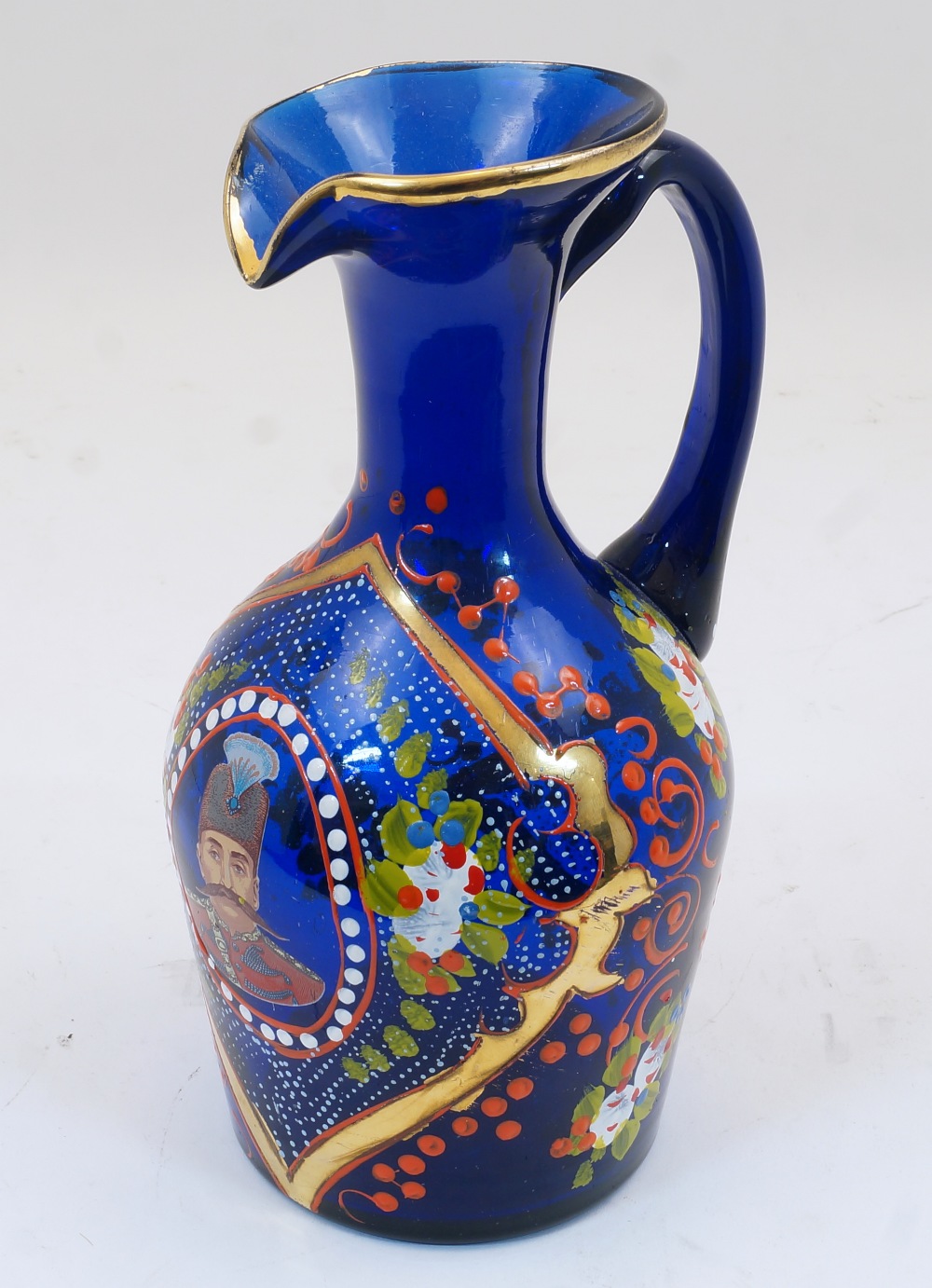 A Bohemian blue glass jug, 19th century, the body enamelled and gilded with foliate motifs and