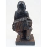 A carved oak figure, early 20th century, depicted seated on a stump and playing the accordion,