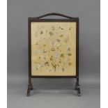 A mahogany fire screen, c.1923, inset with an embroidered panel of flowers and leave, signed L.