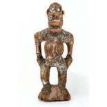 A tribal carved wooden figure of a woman, stood with bent knees and hands held on her hips, with red
