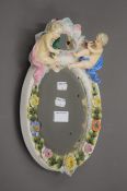 A Continental porcelain mirror mounted with a putto. 32 cm high.