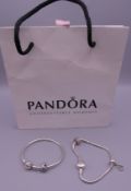 Two silver Pandora bracelets with charms, in a Pandora bag. Both approximately 18 cm long.