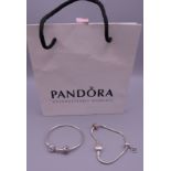 Two silver Pandora bracelets with charms, in a Pandora bag. Both approximately 18 cm long.