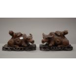 A pair of Chinese carved wooden models of buffalo, each with a child on its back,