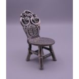 A Chinese white metal model of a chair set with a coin. 8 cm high.