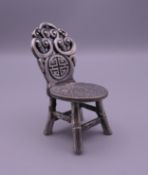 A Chinese white metal model of a chair set with a coin. 8 cm high.