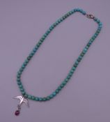A turquoise necklace set with a silver bird pendant. 49 cm long.