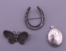 A silver locket, a white metal (silver) horseshoe brooch and a butterfly brooch.