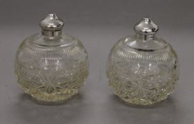 Two round cut glass scent bottles with silver tops, hallmarked Sheffield 1921. 9 cm high.