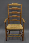 A Philip Clissett rush seated ash and elm ladder back open arm chair. 61 cm wide.