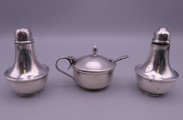 A silver three piece cruet set with a plated spoon.