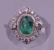 A platinum emerald and diamond ring. Ring size N.