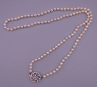 An opera length cultured pearl necklace with a white gold diamond and ruby clasp.
