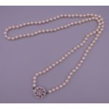 An opera length cultured pearl necklace with a white gold diamond and ruby clasp.