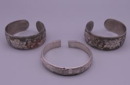 A Chinese silver bangle and two other bangles. The former 7.25 cm wide.