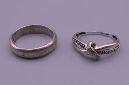 A white gold cross over ring and a silver ring. The former ring size L/M, the latter ring size P.