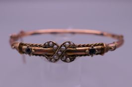 A 9 ct gold sapphire and seed pearl bangle, boxed. 6.5 cm wide. 6 grammes total weight.