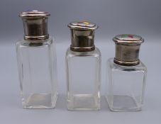 Three silver topped glass scent bottles, each lid set with enamel decoration. 10.