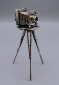 A silver model of a tripod camera. 9 cm high.