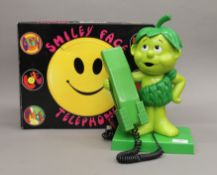 A boxed Smiley Face novelty telephone and a Jolly Green Giant novelty telephone.