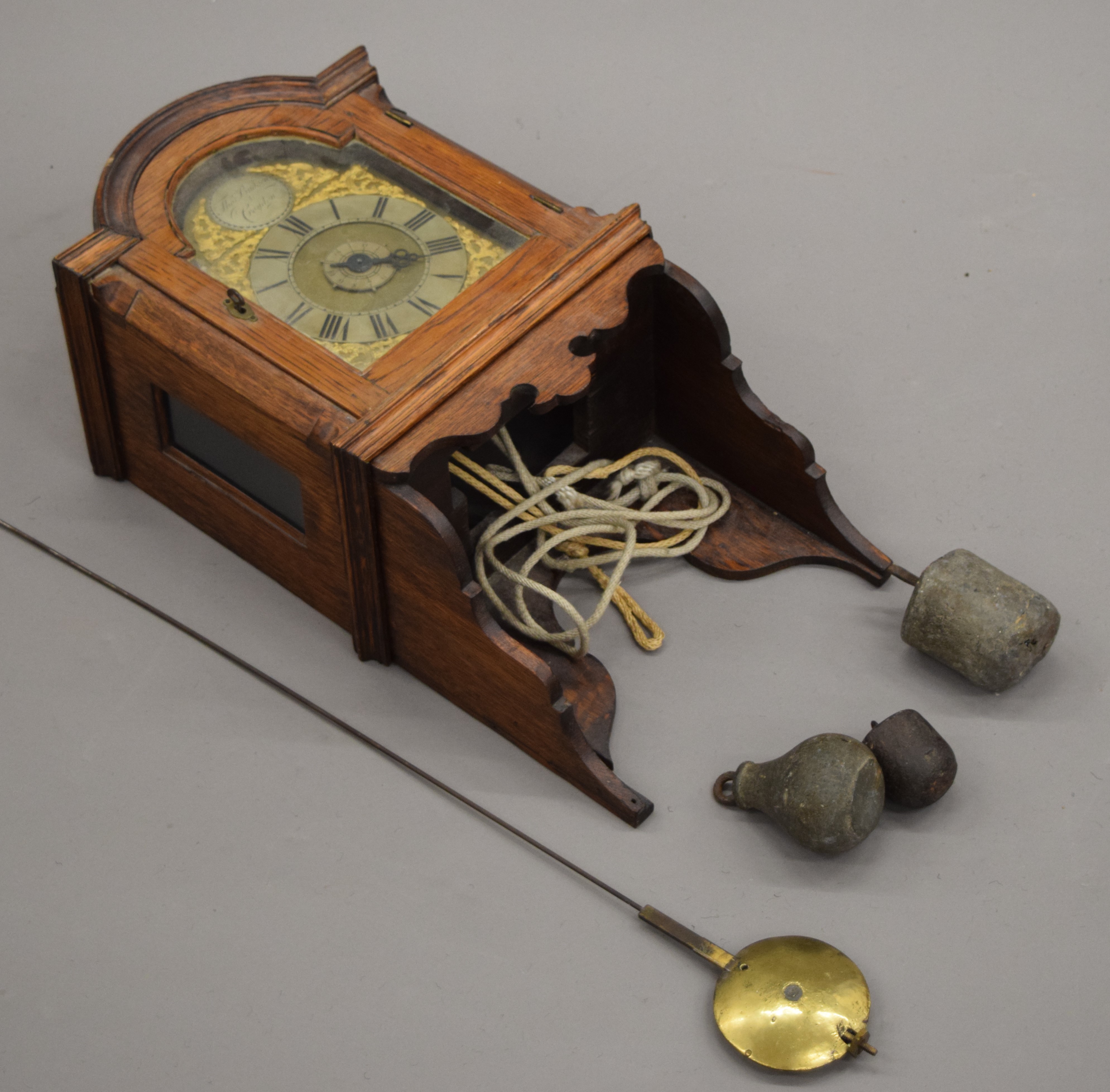 An oak wall clock, the brass dial inscribed Thos Budgen Croydon. 50 cm high.