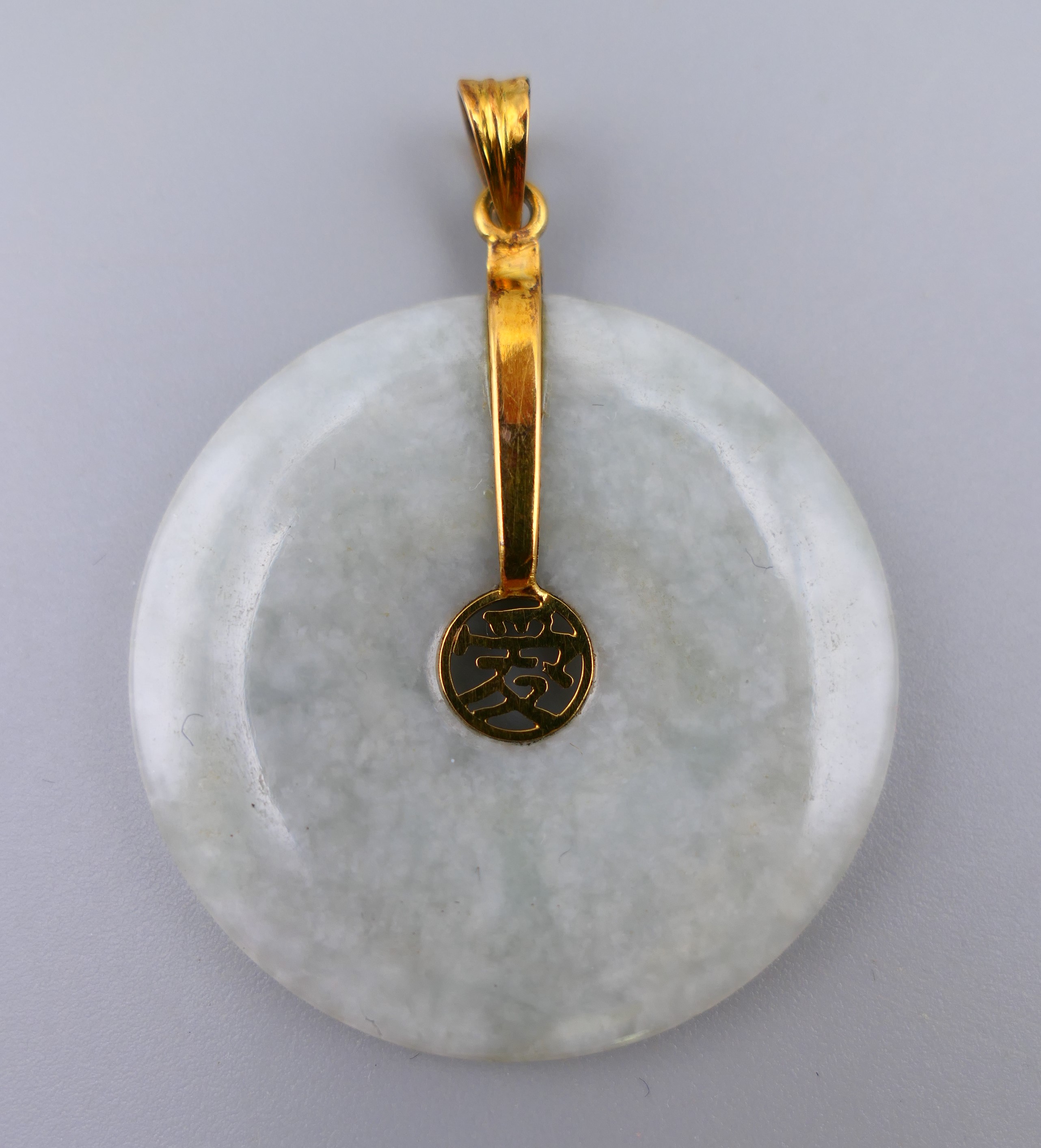 A 14 K gold mounted jade disc pendant. 3.5 cm diameter.