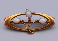 An Art Nouveau 9 ct gold, opal and ruby brooch, boxed. 3.5 cm x 1.5 cm. 1.9 grammes total weight.