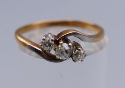 An 18 ct gold and platinum three stone diamond crossover ring. Ring size N. 2.