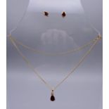 A 9 ct gold garnet pear drop pendant on a gold chain together with a pair of 9 ct gold earrings.